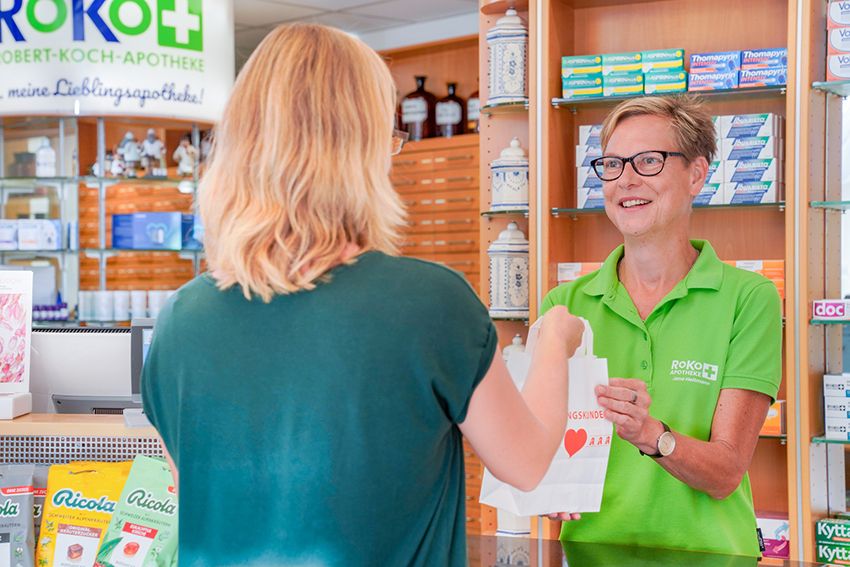 RoKo-Apothekerin übergibt einer Kundin eine Apothekentüte über den Tresen