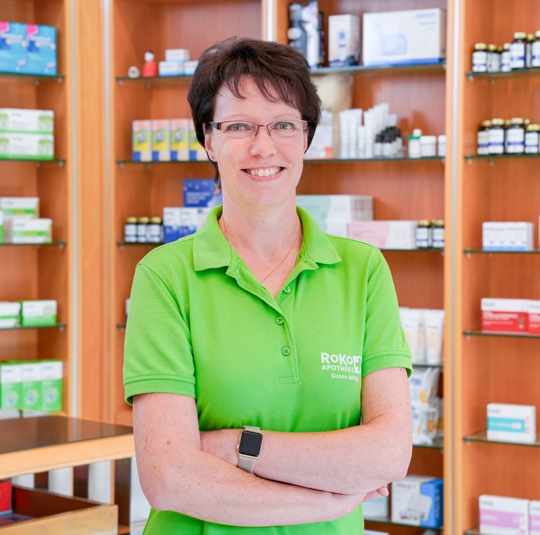 Apothekerin der Robert-Koch-Apotheke im grünen RoKo-Poloshirt vor den Regalen