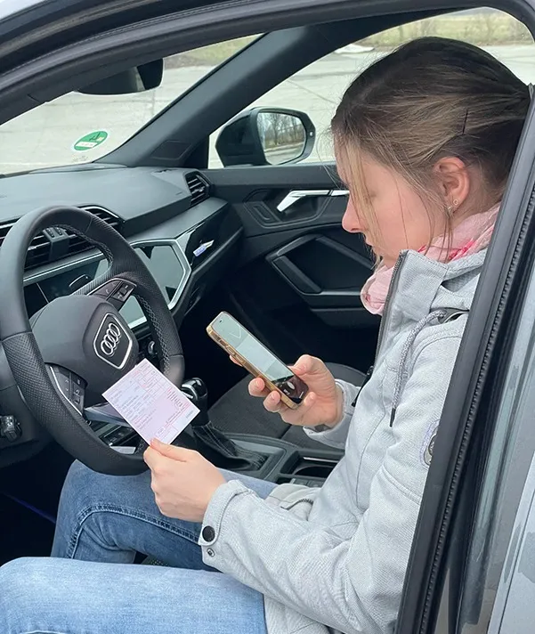 Frau bestellt entspannt im Auto mit dem Smartphone vor – Rezept in der Hand